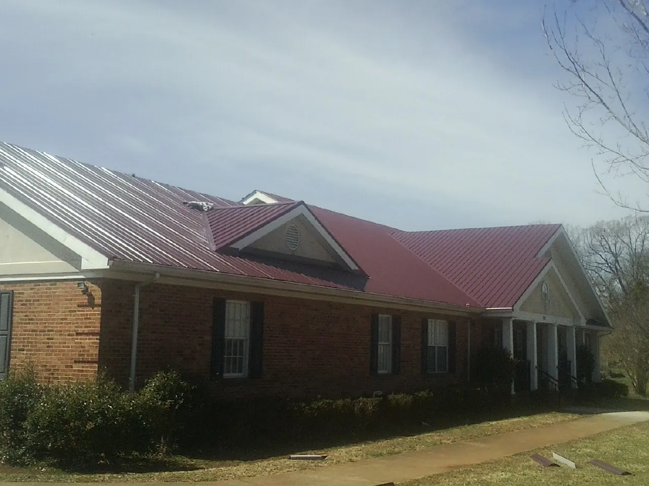 Red metal roof with gabled entries on a long brick building, from a Hail Damage Roof Repair job in Aptos