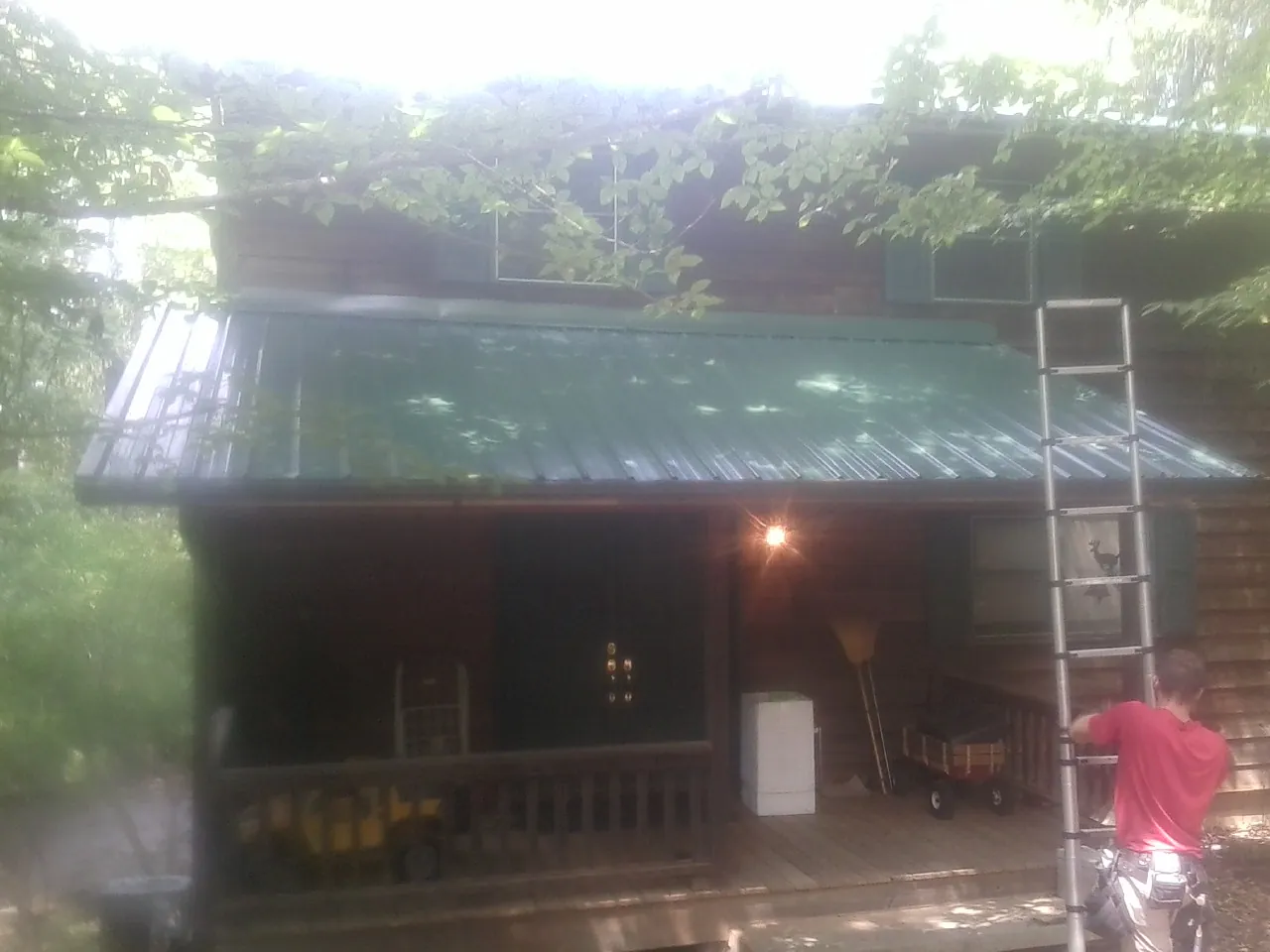Worker on a ladder at the green porch roof of a wooded cabin in Aptos
