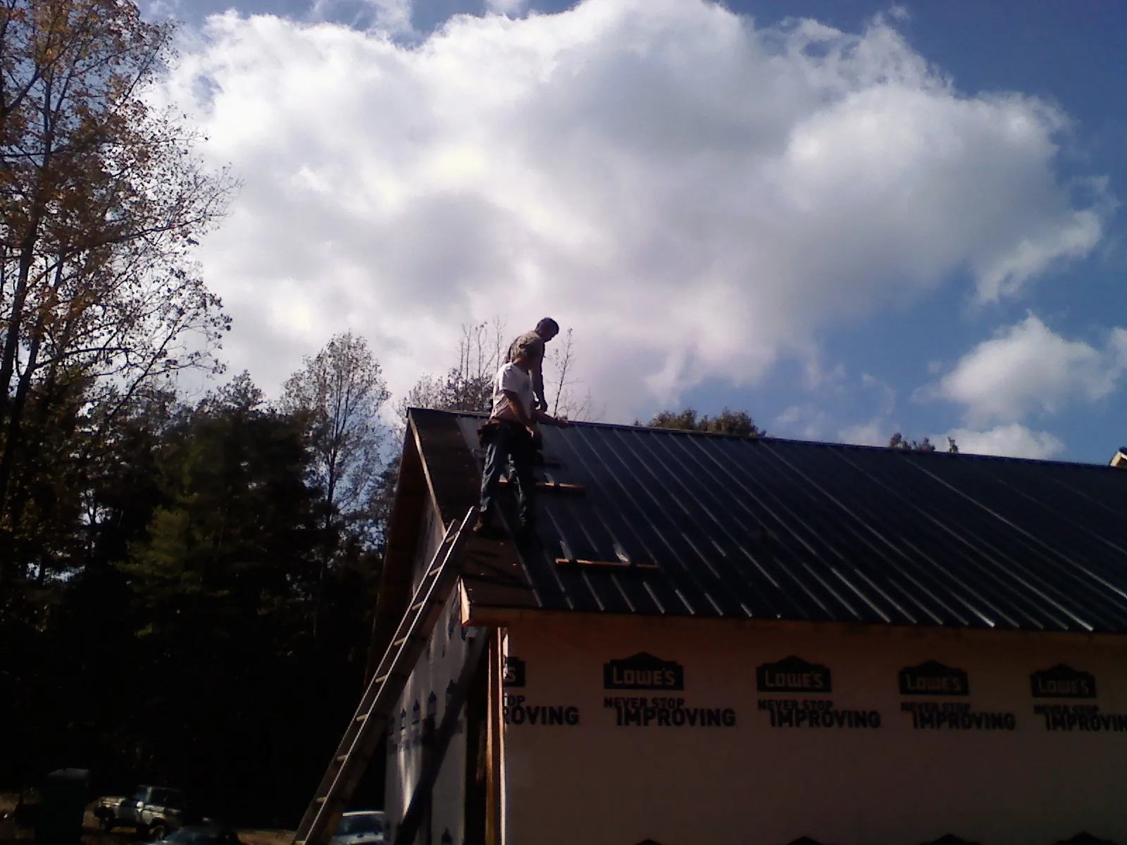 Roofer fastening dark metal panels high against a cloudy sky, from a Roof Inspection job in Aptos