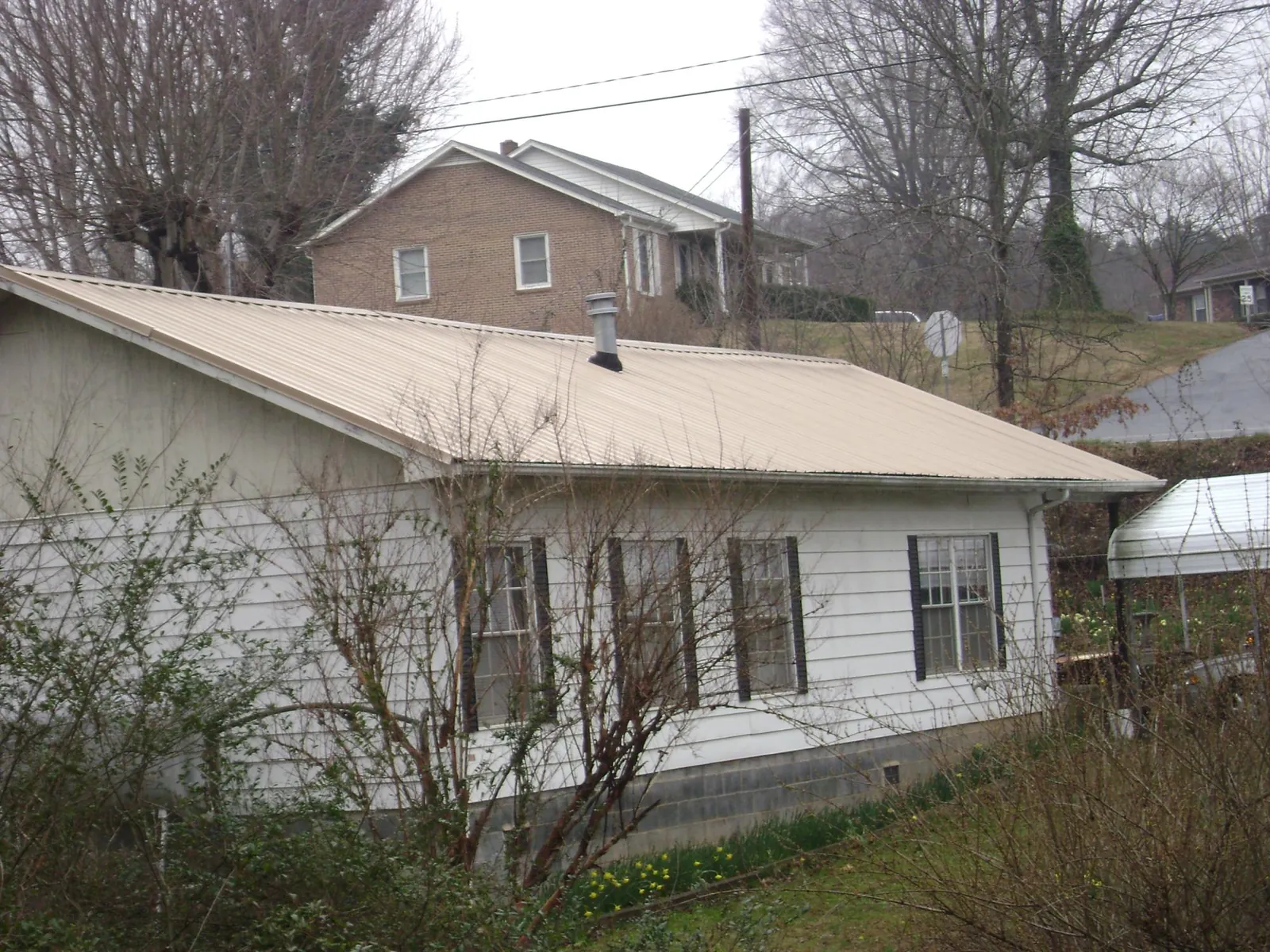 Tan metal roof on a white sided house set into a hillside — Commercial Roofing by Roofing Brothers in Aptos